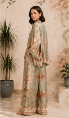 Woman wearing a floral outfit standing in a room with plants and decorative wall.