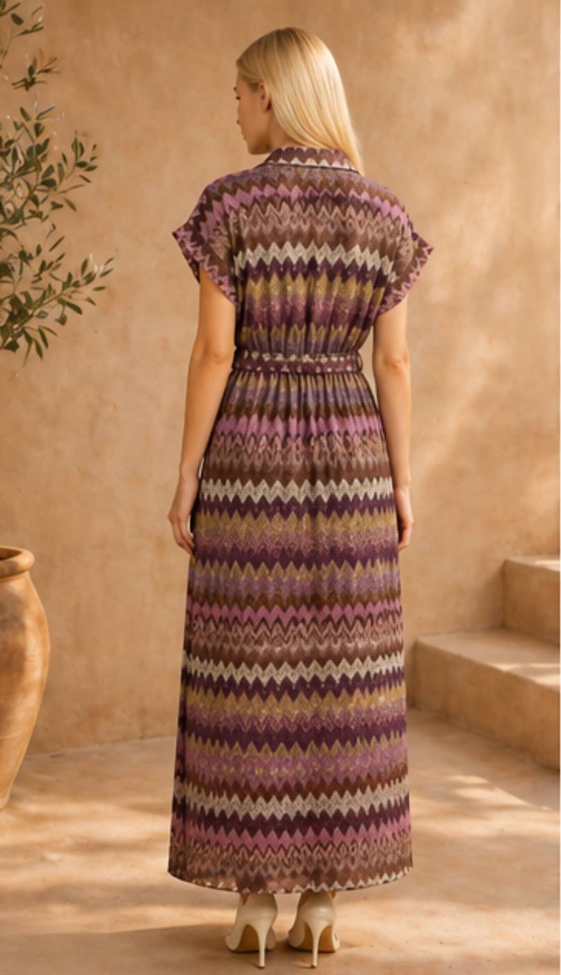 Woman wearing a long, patterned dress standing against a beige wall.