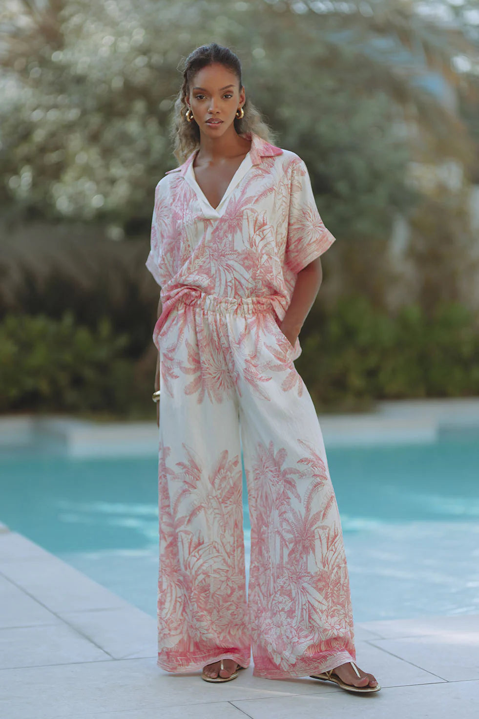 Woman wearing a pink and white floral jumpsuit by a poolside.